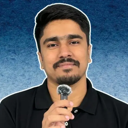 Man holding a small microphone with a fuzzy windscreen against a textured blue background, looking directly at the camera.